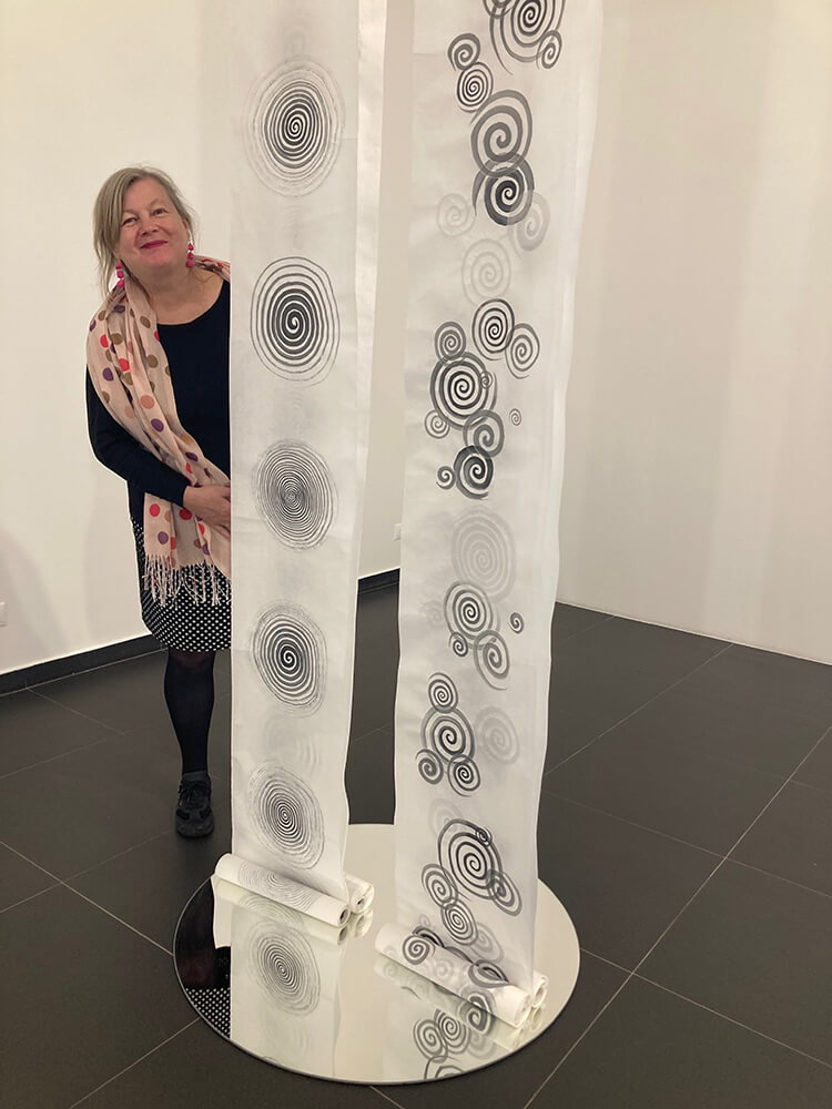 Karin Froehlich neben ihren mit Tusche bemalten Papierbahnen in der Ausstellung in Lettland 